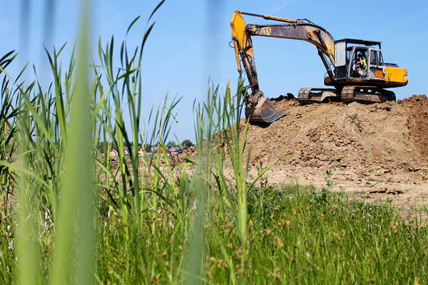 Mid-sized excavator preparing site for new home parked on top of large dirt pile