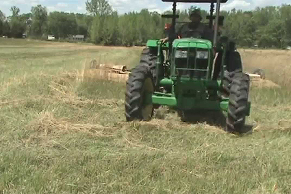 Big John Deere tractor mowing a field with wide bat-wing bush hog attachment