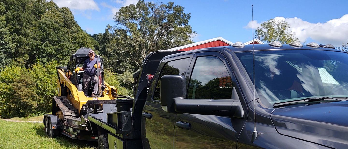 Lyle Foreman climbing out of compact track loader with bushhog attachment at the job site